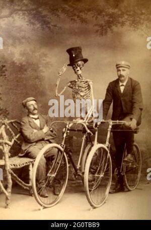 Stravagante fotografia d'epoca - due ciclisti - un uomo e uno scheletro che indossa un cappello sono guardati da un Signore seduto. Foto Stock