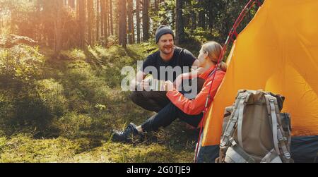 campeggio all'aperto - giovane coppia riposante da una tenda con tazze da tè al campo forestale dopo l'escursione. stile di vita attivo Foto Stock