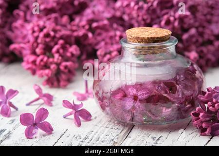 Bottiglia di olio o infusione da fiori lilla su tavola di legno bianco. Foto Stock