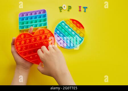Le mani del bambino giocano con il giocattolo colorato pop it fidget. Colorato antistress sensoriale fidget spingere pop esso. Foto Stock