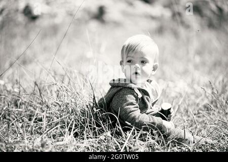 Il bambino piccolo in tute siede sull'erba. Foto in bianco e nero. Primo piano Foto Stock