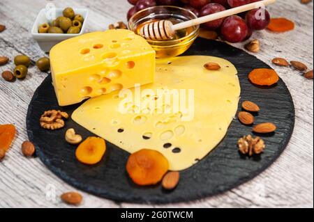 Formaggio con miele, uva e noci su tavola rotonda di grafite Foto Stock