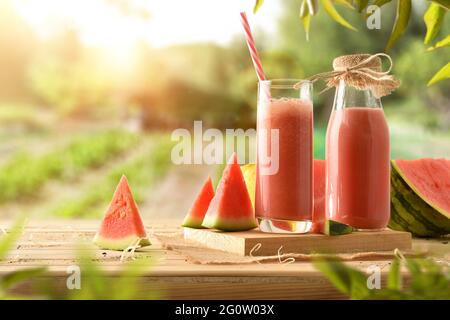Succo di anguria naturale con latte su tavola di legno con frutta tagliata in orto. Vista frontale. Foto Stock