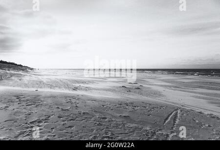 Barche da pesca sulla costa dell'Osstsee sulla spiaggia in Polonia in un aspetto malinconico bianco e nero. Spiaggia sul Mar Baltico con molte impronte. Foto Stock