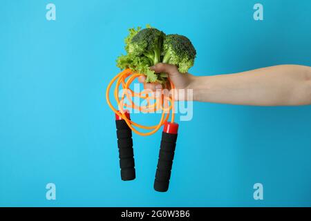 La mano femmina tiene la corda di salto e broccoli su sfondo blu Foto Stock