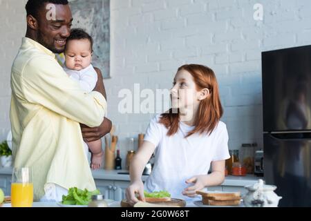 presteen bambino guardando il padre afroamericano con la sorella infantile mentre prepara i panini Foto Stock