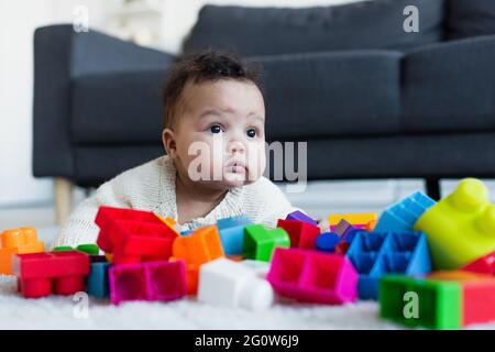 bambina afroamericana strisciando sul pavimento vicino blurred blocchi colorati da costruzione Foto Stock