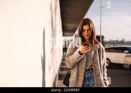 Donna felice che usa lo smartphone che cammina sulla strada in città Foto Stock