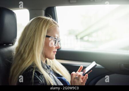 Donna calma che usa lo smartphone sul sedile dell'auto Foto Stock