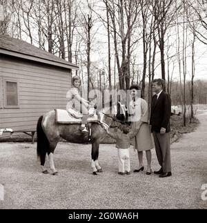 KN-C27672 31 Marzo 1963 Weekend al Camp David. Il presidente John F. Kennedy e la famiglia osservano Caroline Kennedy cavalcando un cavallo di nome "Macaroni" al Camp David. 'Macaroni' indossa una sella marocchina blu e oro, un regalo al presidente Kennedy di Re Hassan II La fotografia include: (L-R) Caroline Kennedy, John F. Kennedy, Jr., First Lady Jacqueline Kennedy, e il presidente Kennedy. Camp David, Maryland. Si prega di credito 'Robert Knudsen. Fotografie della Casa Bianca. John F. Kennedy Presidential Library and Museum, Boston' Foto Stock