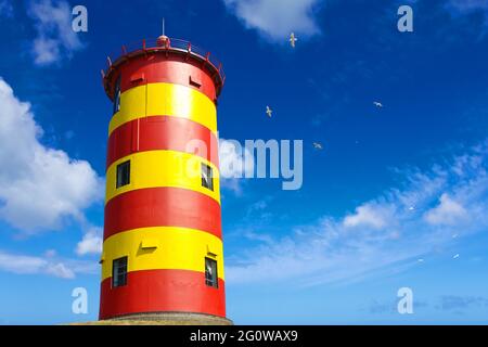 Famoso faro a strisce gialle e rosse Pilsum vicino a Greetsiel, Frisia orientale, Mare del Nord, Germania, contro un cielo blu. Foto Stock