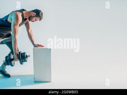 Giovane uomo allenando i muscoli posteriori con manubri Foto Stock