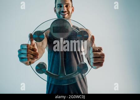 Un sportivo sorridente che mostra le scale di peso alla telecamera Foto Stock