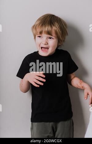 Piccolo carino caucasico ragazzo di 3 anni che indossa una t-shirt nera contro la parete bianca mostrando e ptretendendo è una tigre mentre sorride sicuro e felice. Foto Stock