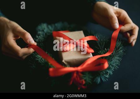 Donna che fa la corona di natale con il pino e il nastro rosso. Idee per la decoriazione di natale. Sfondo di Natale. Foto Stock