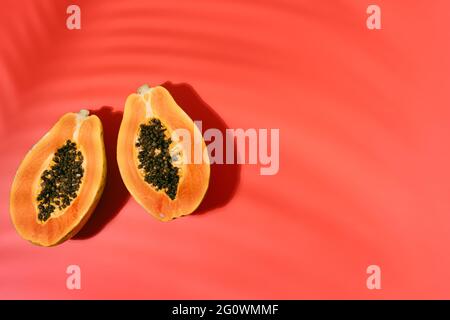Papaya fresca con semi neri su sfondo rosso con ombre di foglie di cocco in estate. Concetto di vacanza e natura. Spazio copia. Vista dall'alto Foto Stock