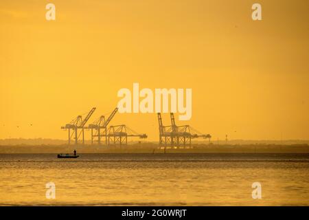 Un pescatore tenta la sua fortuna al tramonto sulla baia di Mobile in Alabama, Stati Uniti, con i cantieri navali in Mobile in aumento sullo sfondo. L'immagine è stata acquisita Foto Stock