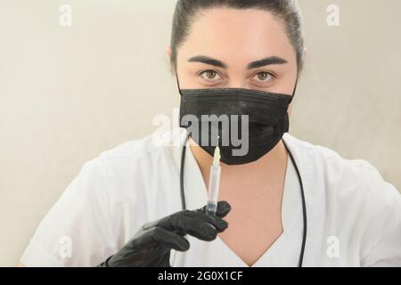 Ritratto donna caucasica medico tiene e prepara una siringa per la procedura medica o l'iniezione di bellezza. Mettere a fuoco gli occhi. Foto Stock