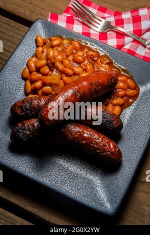 Bratwurst alla griglia con fagioli cowboy di pancetta sul tavolo da picnic Foto Stock