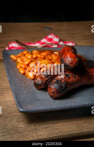 Bratwurst alla griglia con fagioli cowboy di pancetta sul tavolo da picnic Foto Stock