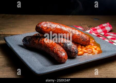 Bratwurst alla griglia con fagioli cowboy di pancetta sul tavolo da picnic Foto Stock