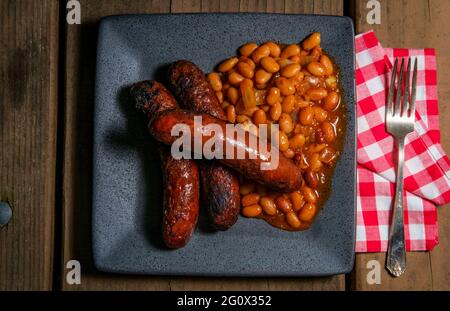 Bratwurst alla griglia con fagioli cowboy di pancetta sul tavolo da picnic Foto Stock