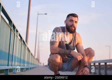 L'uomo tatuato, barbuto che ha una pausa durante il suo allenamento di strada Foto Stock