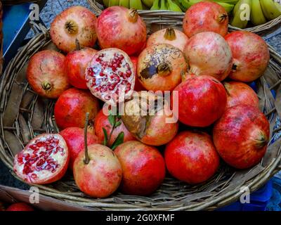 Un grande cestino rustico pieno di melograne fresche mature succose aperte e chiuse per la vendita su un mercato locale di strada. Foto Stock