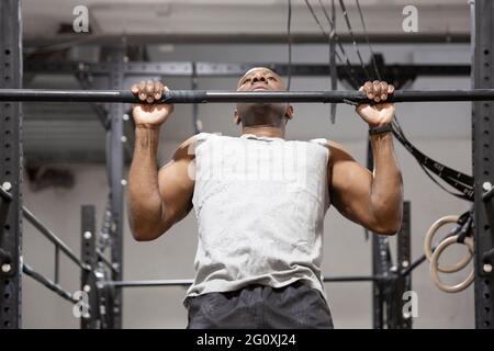 Sportivo afroamericano che fa esercizio fisico su bar fisso. Allenamento fitness in palestra. Foto Stock