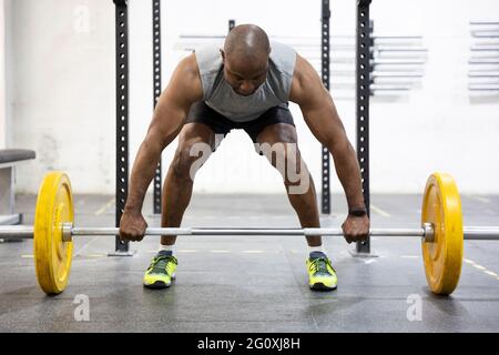 Vista frontale di un forte atleta africano-americano che si prepara per il sollevamento pesi in palestra. Foto Stock