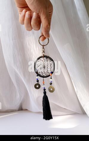 Foto di mano che tiene un mini dreamcatcher con sfondo di una tenda bianca Foto Stock