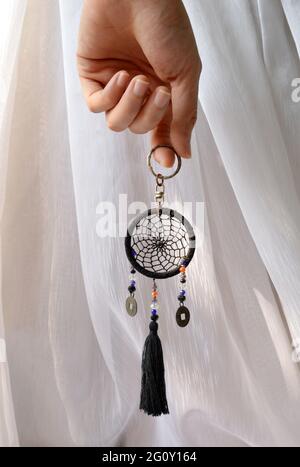 Foto di mano che tiene un mini dreamcatcher con sfondo di una tenda bianca Foto Stock