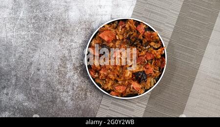 Bigos - tradizionale piatto di smalto di crauti stufati con prugne e salsicce su un piatto rotondo su sfondo grigio scuro. Vista dall'alto, disposizione piatta Foto Stock