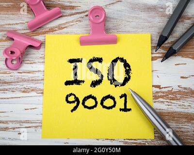 Standard di qualità ISO 9001. Foglio giallo di carta e matite su un tavolo di legno. Foto Stock