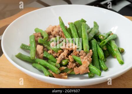 Primo piano su cowpeas fritti in padella o fagioli dagli occhi neri con maiale tritato con aglio e salsa di soia, cibo nel disco bianco sul tagliere in cucina, come Foto Stock