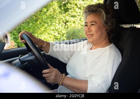 Donna anziana asiatica sorridente durante la guida dell'auto Foto Stock