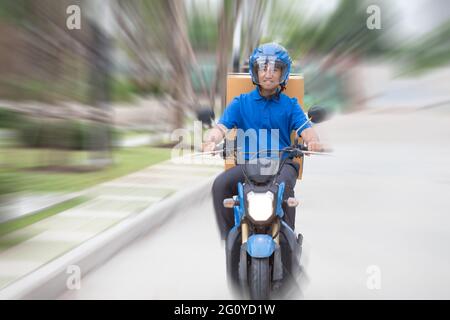 Consegna ragazzo su scooter con scatola di pacchi che guida veloce in fretta. Corriere che consegna espresso con moto Foto Stock