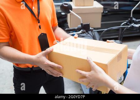 Donna mano accetta una consegna di scatole da deliveryman, consegnare merci in motocicletta, servizio veloce e trasporto gratuito Foto Stock