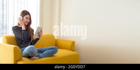 Asian teen girl indossa le cuffie lingua di apprendimento online guardando lo schermo tablet durante la chiusura della scuola e la necessità di prendere le distanze sociali. Casa Foto Stock