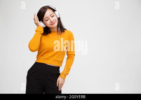 Bella giovane donna asiatica con cuffie che ascoltano la musica outfit luminoso godendo la melodia della canzone isolata su sfondo bianco Foto Stock