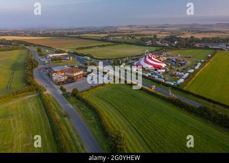 Un agricoltore tende al suo campo in un trattore, mentre un Circus si imposta accanto al Blue Dolphin Holiday Park e il Plough Pub Aerial Images Drone Air Filey Foto Stock