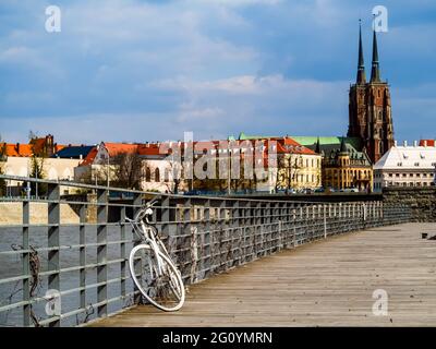 Bicicletta bianca retrò abbandonata sul molo in legno della città con vista sulla città vecchia. Wroclaw, Polonia Foto Stock