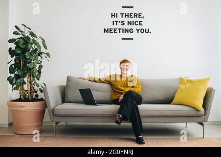 Happy executive femminile sul divano nella hall dell'ufficio. Una donna d'affari allegra che siede nella lobby. Foto Stock