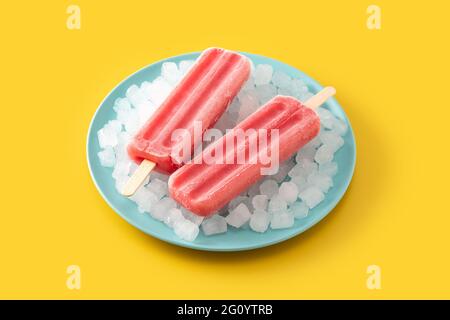 Popsicle di fragole con ghiaccio su sfondo giallo Foto Stock