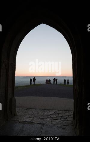 I visitatori di Glastonbury Tor aspettano che il sole salisca all'alba a fine Spring Somerset, Inghilterra Foto Stock