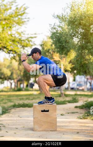 Uomo adulto forte che indossa abiti sportivi utilizzando jumping box nel parco e allenarsi. Foto Stock