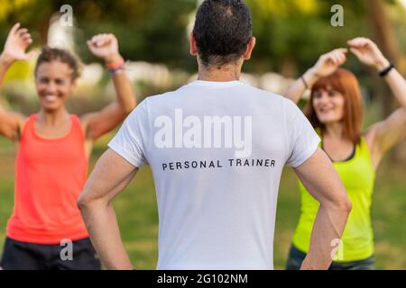 Allenatore di fitness maschile facendo allenamento nel parco con due donne felici. Foto Stock