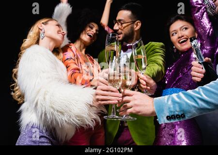 felici amici interrazziali che si aggrappano con bicchieri di champagne su sfondo nero Foto Stock