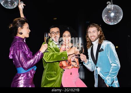 felici amici multirazziali che ballano con bicchieri di champagne su sfondo nero Foto Stock