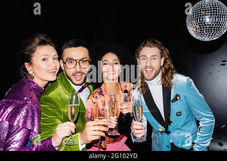 felici amici multirazziali che bevono toasting con bicchieri di champagne su sfondo nero Foto Stock